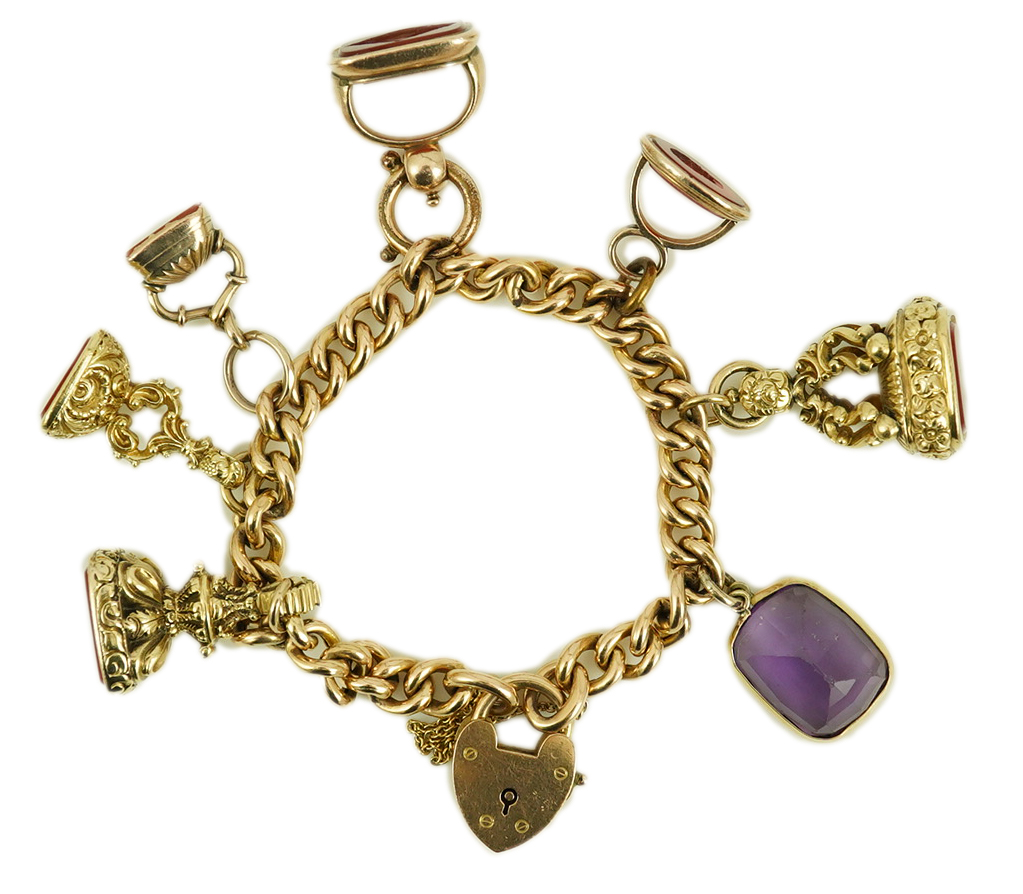 An Edwardian 15ct gold curb link charm bracelet with heart shaped padlock clasp, hung with six assorted gold overlaid and carnelian set fob seals